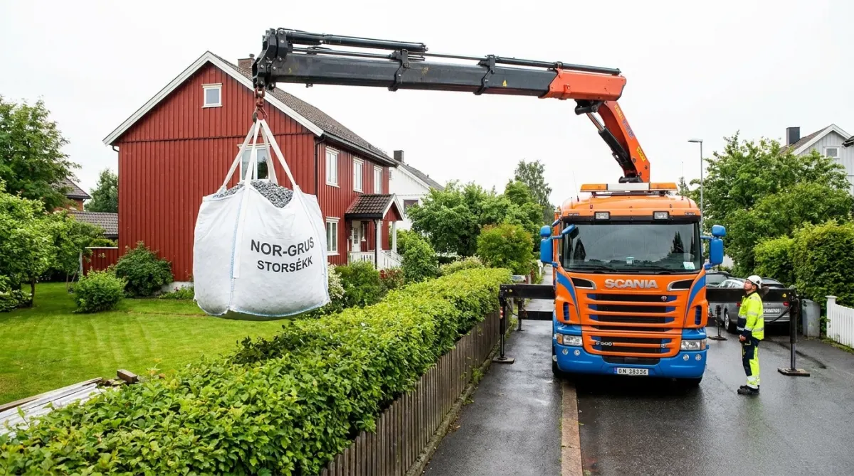 Kranbil leverer big bag storsekk med pukk over hekken til en hage i Oslo